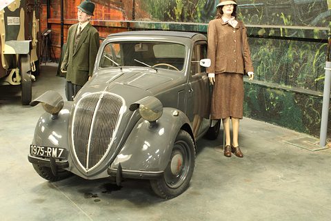 Grey small saloon with mannequins in 1940 clothes standing beside it in a painted scene. Opens a larger view