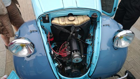 Small four-cylinder engine with its fuel tank above, under a raised pale blue bonnet. Opens a larger view