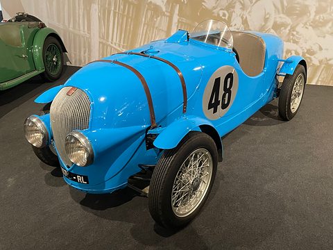 Light blue open racing two-seater with strapped bonnet, wire wheels and a big 48 on its side.
