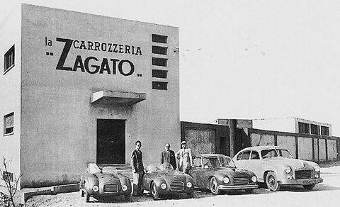 Black and white: men standing beside small sports cars in front of a building lettered CARROZZERIA ZAGATO. Opens a larger view