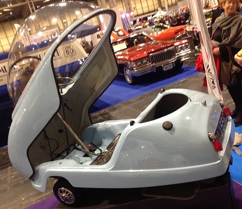 Pale blue bubble car side-on with its canopy lifted, showing the bench seat and controls. Opens a larger view