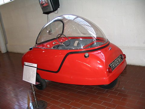 Red bubble car side-on on a red tiled floor, an information card on a stand beside it. Opens a larger view