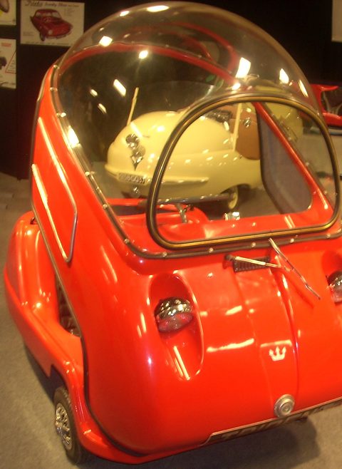 Red bubble car with its door-like front panel and dome, seen from above on a grey carpet. Opens a larger view