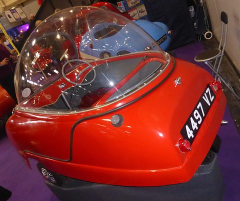 Red bubble car from behind on a purple plinth, its plate set at an angle on the tail. Opens a larger view