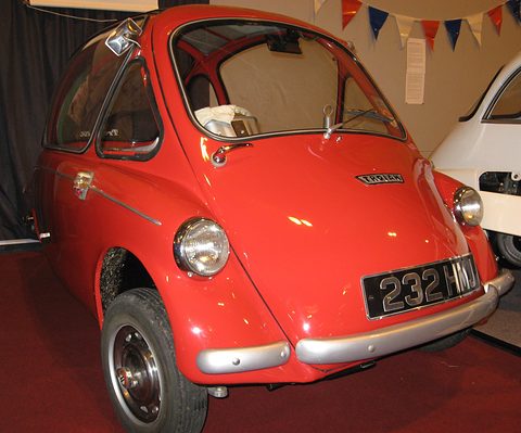Red bubble car on a red carpet in front of bunting, seen close from the front right. Opens a larger view