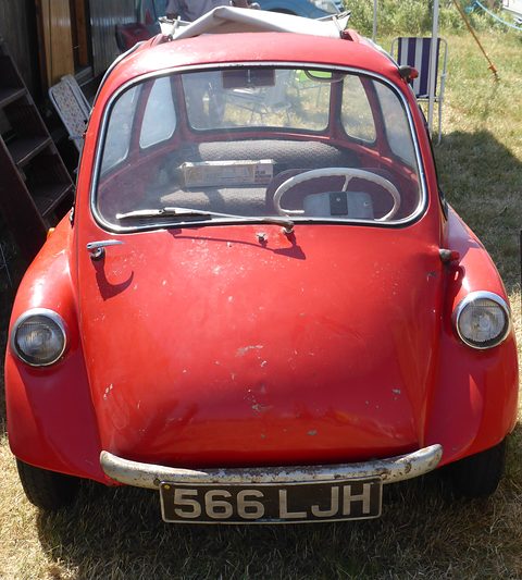 Red bubble car seen from the front on dry grass, its roof open. Opens a larger view