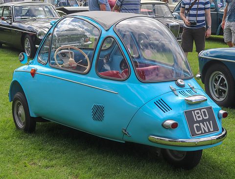 Turquoise bubble car seen from the rear right on grass, its tail tapering to a single wheel. Opens a larger view