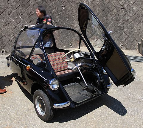 Black bubble car with its whole front opened upwards, revealing a tartan seat and the steering wheel