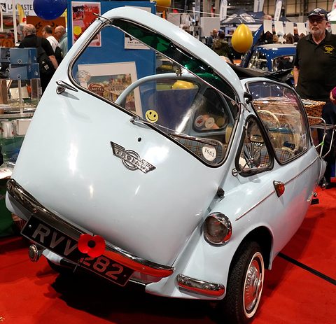 White-blue bubble car with its front door raised on a red carpet, visitors behind. Opens a larger view