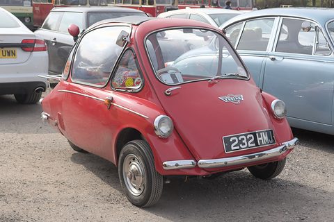 Red bubble car on a gravel car park beside a pale Jaguar. Opens a larger view