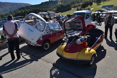Two bubble cars side by side with their canopies and doors raised, people standing around. Opens a larger view