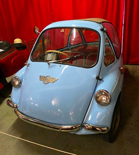Pale blue bubble car seen from the front against red curtains. Opens a larger view