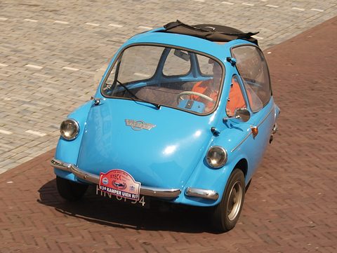 Blue bubble car with its roof rolled back on herringbone brick paving, seen from above