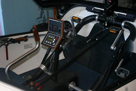 Switch panel with rocker switches beside a steering joystick, handlebar grips, pedal crank and white side panels. Opens a larger view