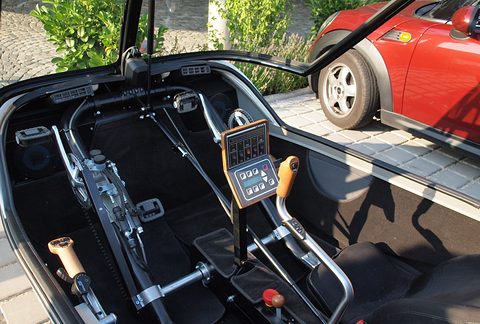 Two black seats either side of a steering joystick with a keypad display, pedal cranks and gear levers below.