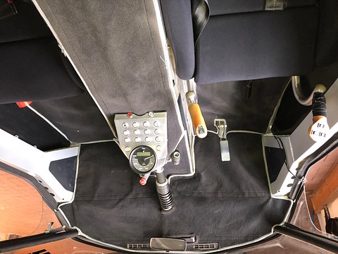 Looking down into a cockpit with two seats, a keypad and round display, pedals and grey carpet. Opens a larger view