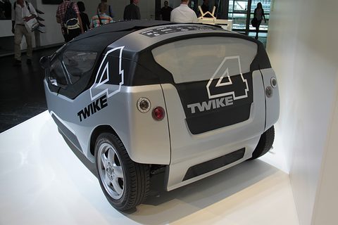 Rear of a silver and black two-seater with TWIKE 4 lettering and round lamps, visitors behind. Opens a larger view