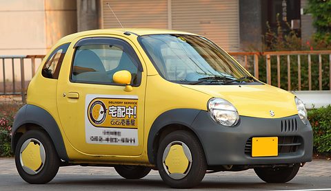 Yellow tiny two-seat hatchback with a grey lower body and a delivery-service sign on its door.