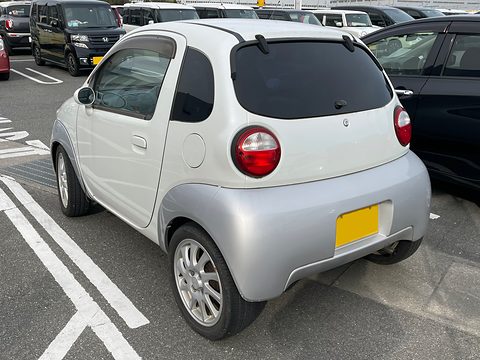 Rear of a white and silver tiny hatchback with round tail lamps and alloy wheels in a marked bay. Opens a larger view