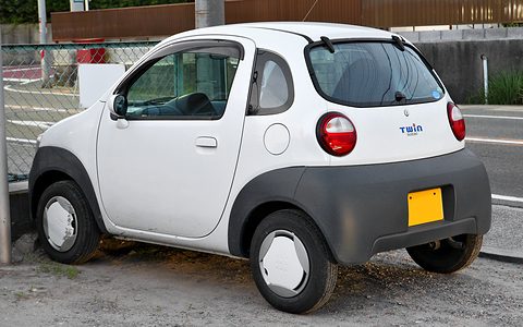 Rear of a white tiny hatchback with a glass hatch, round tail lamps and a grey lower body.