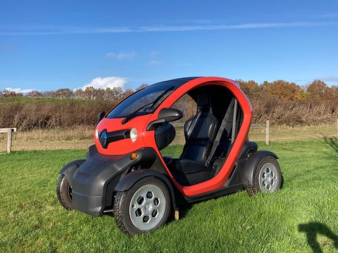 Red and black tandem two-seater with black seats parked on grass under a blue sky.