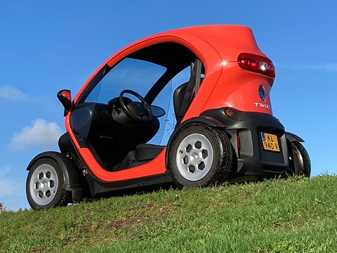 Rear of a red tandem two-seater with a Dutch plate, seen from below on a grass slope against blue sky. Opens a larger view