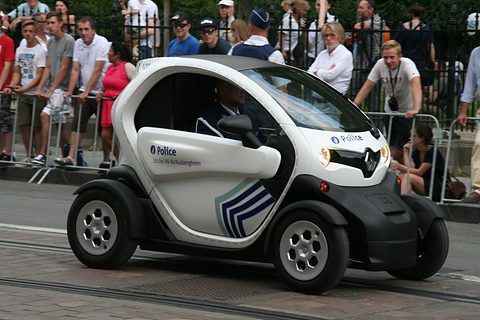 White tandem two-seater with Police lettering and blue stripes driving past spectators behind barriers. Opens a larger view