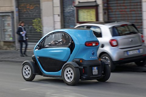 Blue and black tandem two-seater driving along a street past a silver Smart and shuttered shops. Opens a larger view