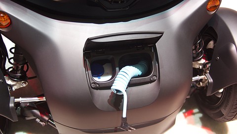 Close view of a Twizy’s nose with a flap open and a coiled pale blue cable plugged into the socket. Opens a larger view