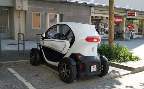 White and black tandem two-seater parked in a marked bay by a planter and a shopfront. Opens a larger view