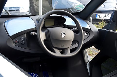 Black steering wheel with a Renault badge, a small digital display and grey dashboard panels. Opens a larger view