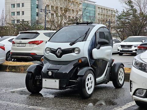 White and black tandem two-seater with a blanked plate parked on wet tarmac among SUVs. Opens a larger view