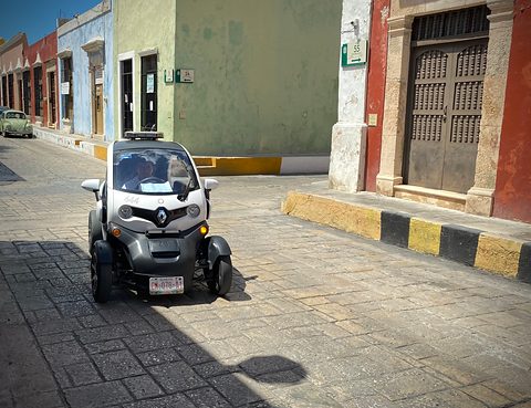 White and black tandem two-seater with a roof light driving along a colonial street with coloured houses. Opens a larger view