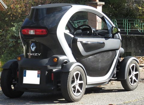Rear of a white and black tandem two-seater with a TWIZY badge, parked by a green railing. Opens a larger view