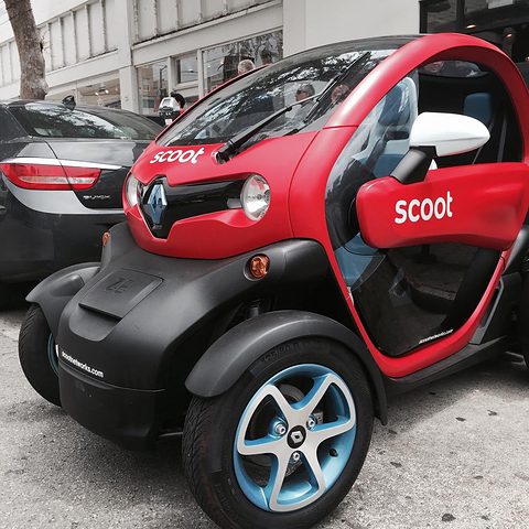 Red and black tandem two-seater with Scoot lettering and blue wheels parked at a kerb. Opens a larger view