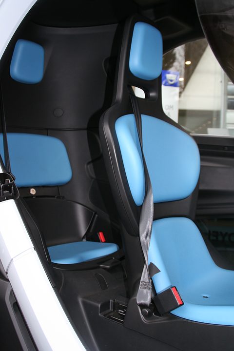 Two blue and black seats one behind the other inside a narrow car, seen through the open door.