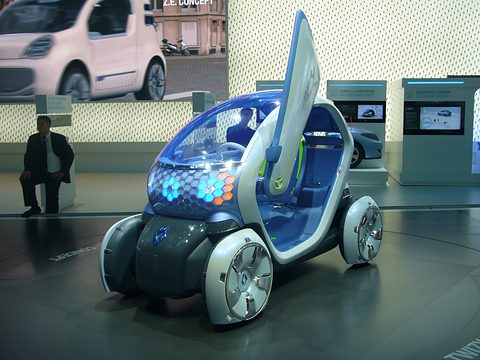 White and blue tandem two-seat concept with glowing orange honeycomb lights and its door swung up, on a show floor. Opens a larger view
