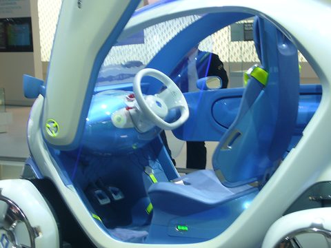 Blue interior with a white steering wheel, a front seat and a rear seat behind it, framed by the open door. Opens a larger view