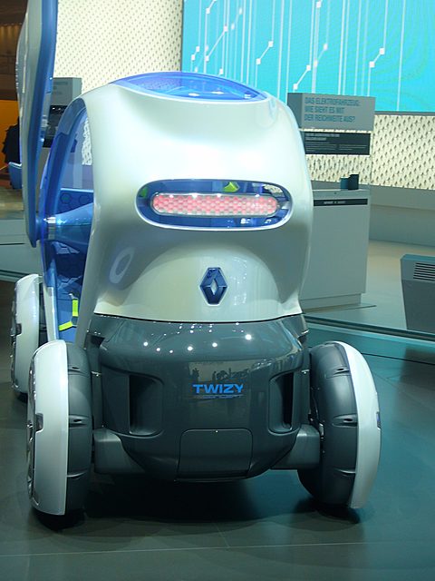Rear of a white and blue narrow concept car with a pink honeycomb tail lamp and a TWIZY plate. Opens a larger view
