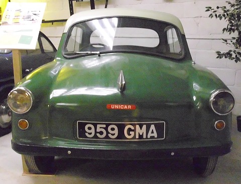 Dark green microcar with cream roof, registration 959 GMA, seen from the front in a museum. Opens a larger view