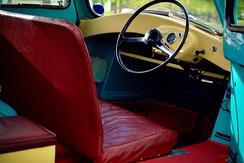Red leather bench seat folded forward in front of a large steering wheel and cream painted dashboard. Opens a larger view