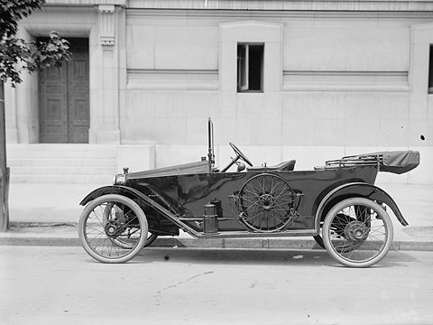 Side view of a small black open tourer with a spare wire wheel on its flank, standing in a quiet street.