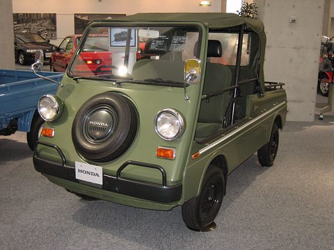 Olive green doorless small utility with a spare wheel on its nose between round headlamps and a canvas top, on a museum floor. Opens a larger view