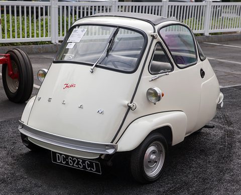 Small white egg-shaped car with a front-opening door, Isetta script and French plate DC-623-CJ, a white fence behind.