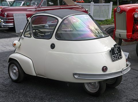 Back of a white bubble car with a wide rear window and chrome bumper, a red tractor beside it.