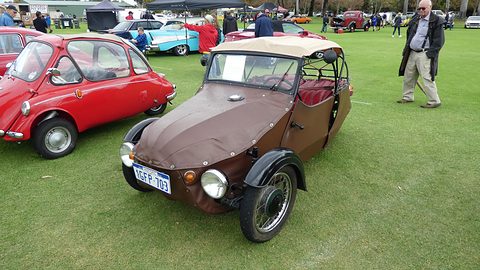 Brown leatherette three-wheeler with beige hood and black wings, Velorex script, next to a red bubble car. Opens a larger view