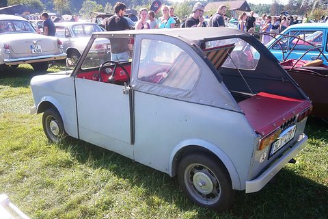 Rear of a grey two-door microcar with folded fabric roof, red rear deck and Czech plate, among show visitors. Opens a larger view