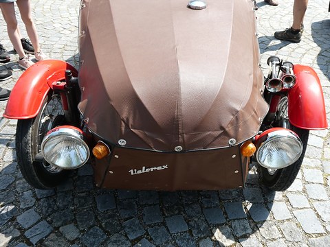 Close view down onto a brown leatherette bonnet between two red wings, chrome headlamps and twin horns. Opens a larger view