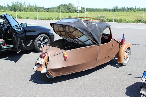 Brown three-wheeler with the black rear hood and padded cover hinged up, twin silencers and Czech plate. Opens a larger view