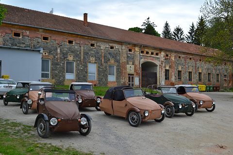Six brown, tan and green three-wheelers parked on gravel in front of a long old stone building. Opens a larger view